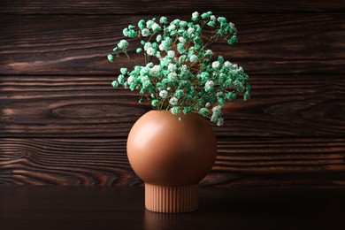 Photo of Beautiful dyed gypsophila flowers in stylish vase on wooden table