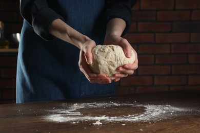 Photo of Making bread. Woman kneading dough at wooden table indoors, closeup