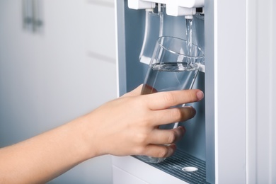 Photo of Woman filling glass with water cooler indoors, closeup. Refreshing drink