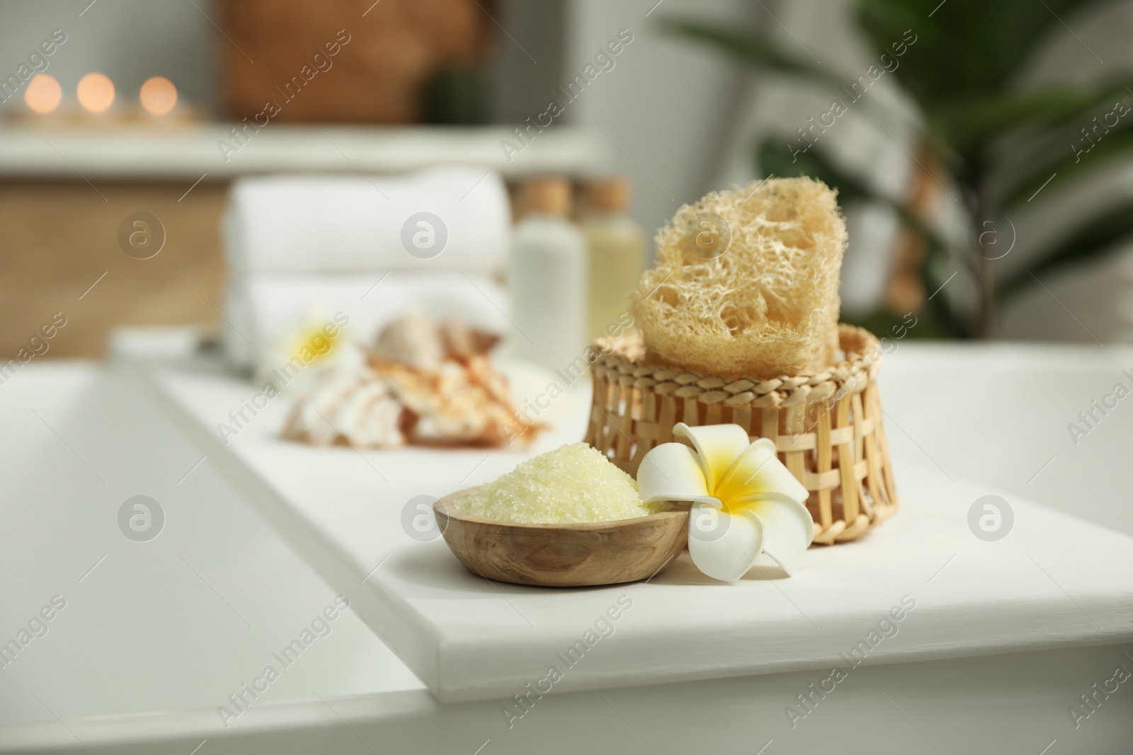 Photo of Bath tray with spa products and plumeria flower on tub in bathroom, space for text