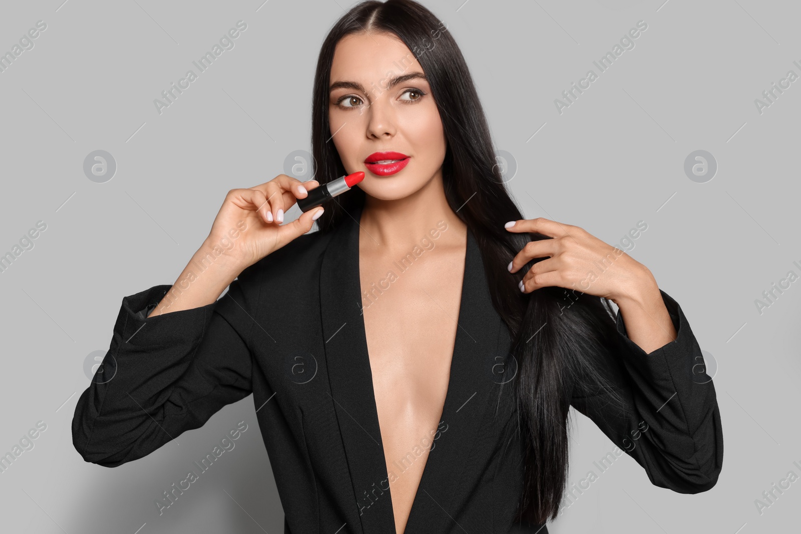 Photo of Young woman with beautiful makeup holding red lipstick on light gray background