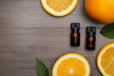 Bottles of essential oil with orange slices and leaves on wooden table, flat lay. Space for text