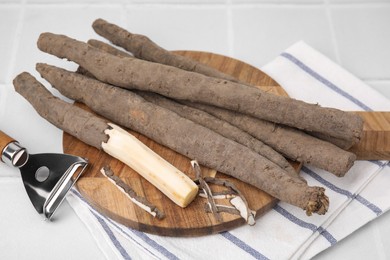 Photo of Raw salsify roots and peeler on white tiled table