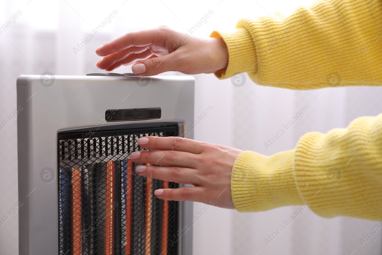 Photo of Woman warming hands near heater indoors, closeup