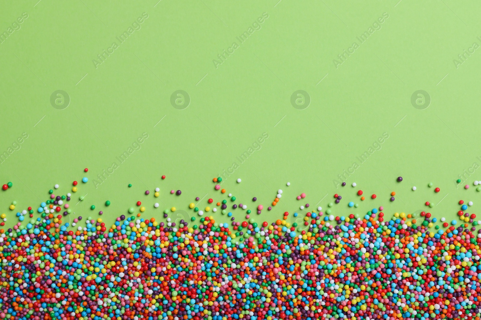 Photo of Colorful sprinkles on green background, flat lay with space for text. Confectionery decor