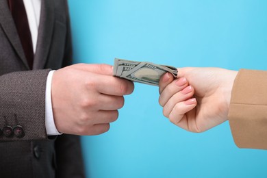 Photo of Man giving money to woman on light blue background, closeup. Currency exchange