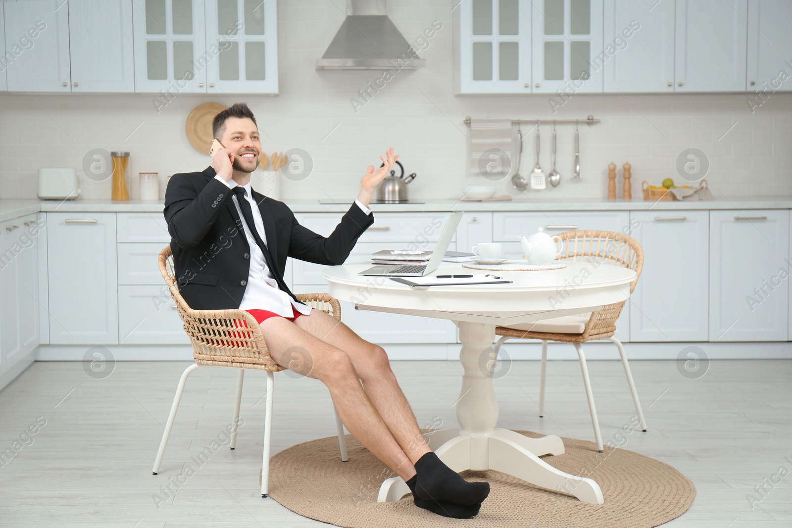 Photo of Businessman in shirt and underwear talking on phone while working with laptop at home