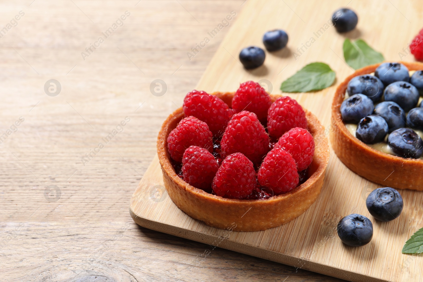 Photo of Tartlets with different fresh berries on wooden table, space for text. Delicious dessert