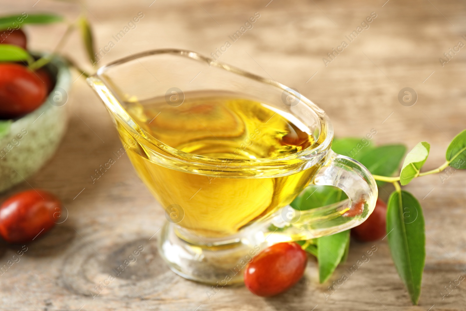 Photo of Glass sauce boat with jojoba oil and seeds on wooden table