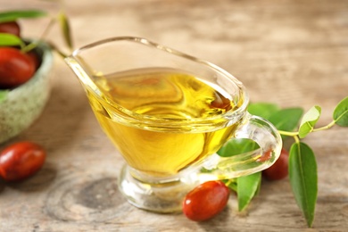 Glass sauce boat with jojoba oil and seeds on wooden table