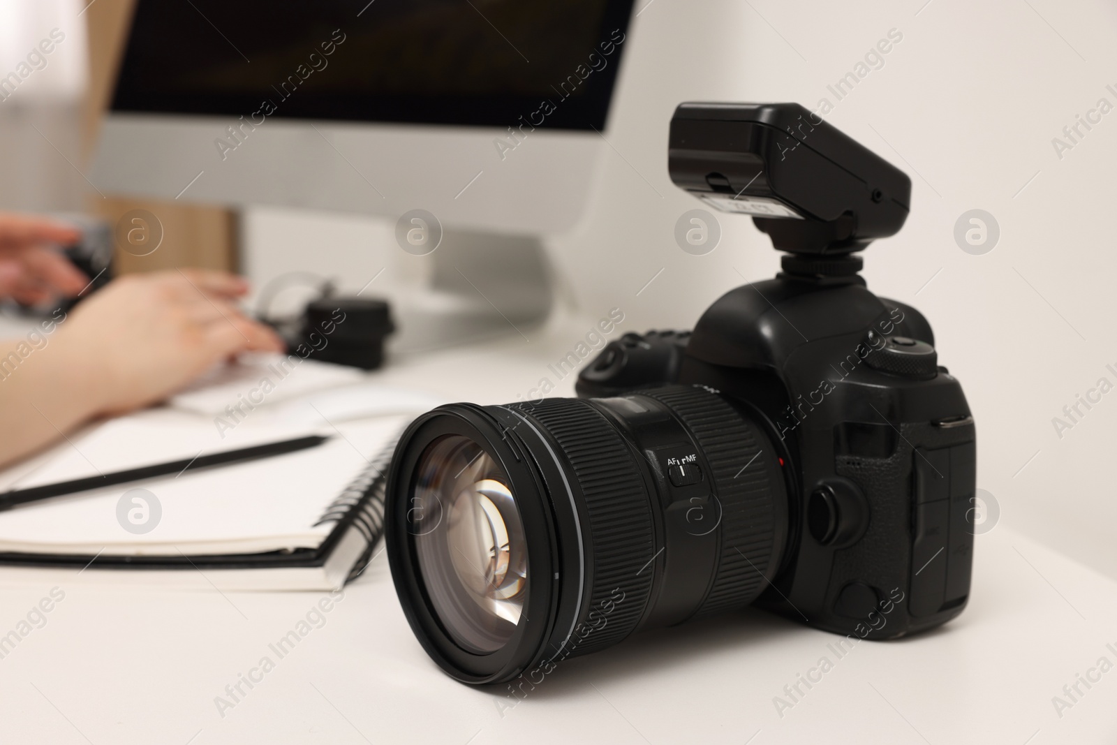 Photo of Photographer working on computer at white table with camera indoors, closeup