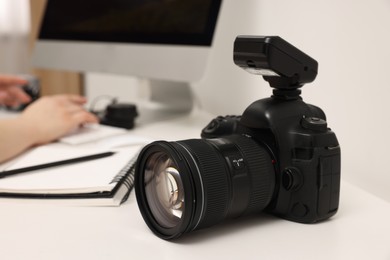 Photographer working on computer at white table with camera indoors, closeup