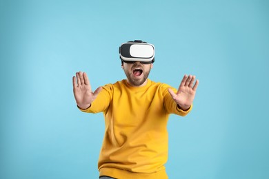 Photo of Emotional man using virtual reality headset on light blue background