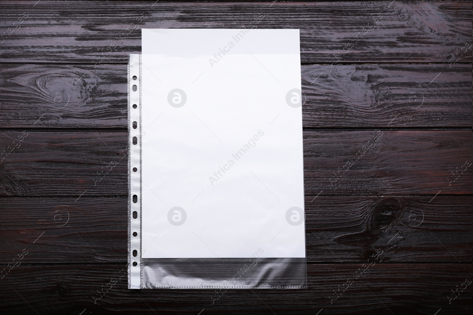 Photo of Punched pocket with paper sheet on brown wooden table, top view. Space for text