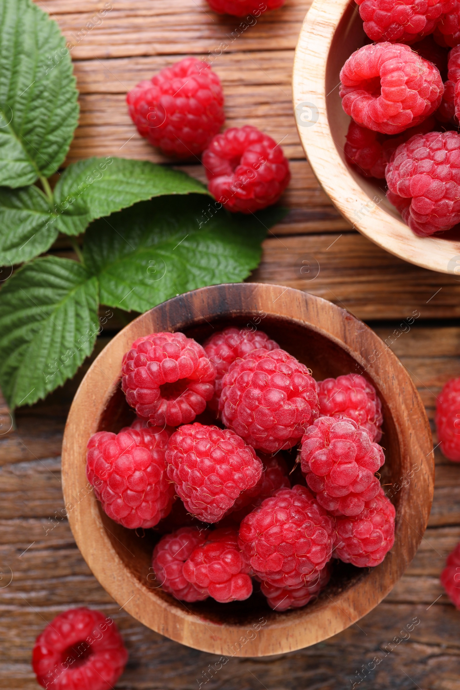 Photo of Tasty ripe raspberries and green leaves on wooden table, flat lay