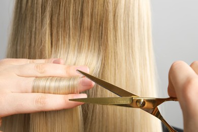 Hairdresser cutting client's hair with scissors on light grey background, closeup