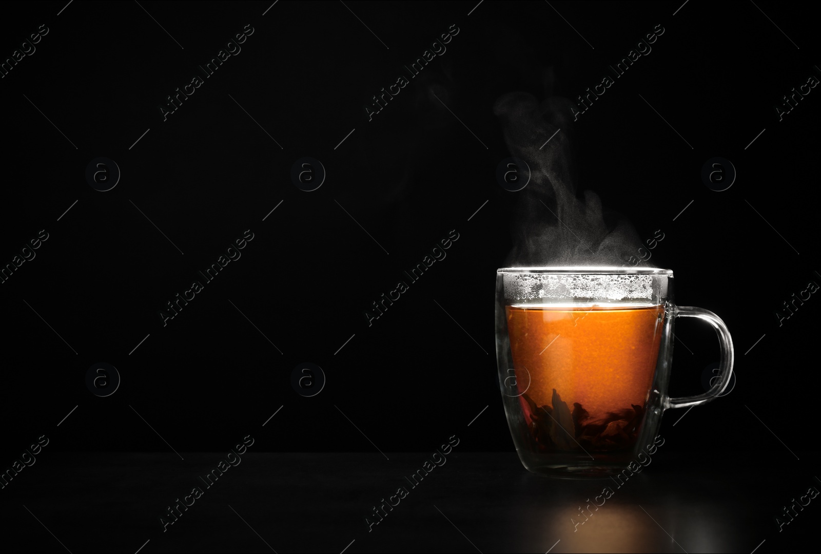 Photo of Glass cup of hot leaf tea on table against black background, space for text