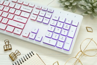 Photo of Modern RGB keyboard and eyeglasses on white wooden table