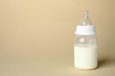 Photo of Feeding bottle with infant formula on beige background. Space for text
