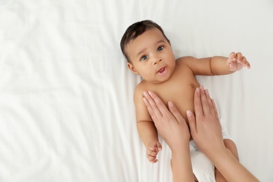 Top view of mother and her cute child on white bed, space for text. Baby massage and exercises