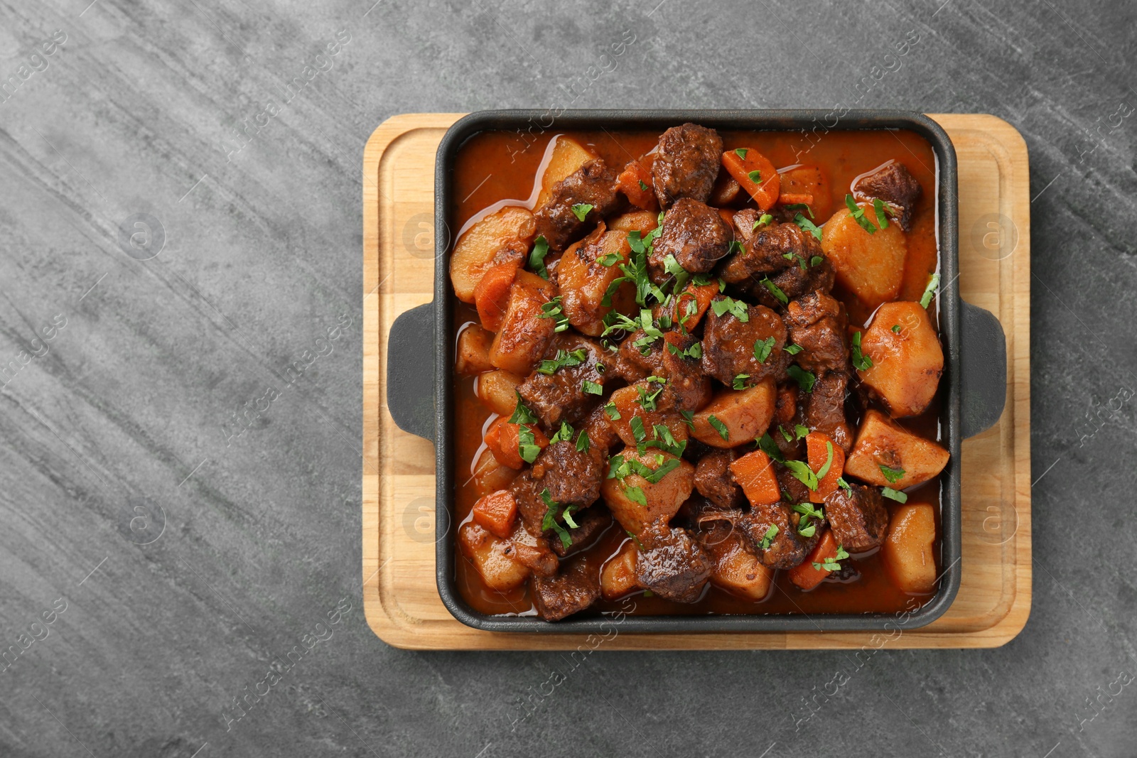 Photo of Delicious beef stew with carrots, parsley and potatoes on grey table, top view. Space for text