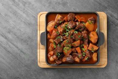 Photo of Delicious beef stew with carrots, parsley and potatoes on grey table, top view. Space for text