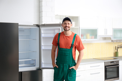 Photo of Male technician in uniform near refrigerator indoors