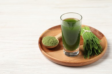 Photo of Wheat grass drink in shot glass, spoon of green powder and fresh sprouts on white wooden table, space for text