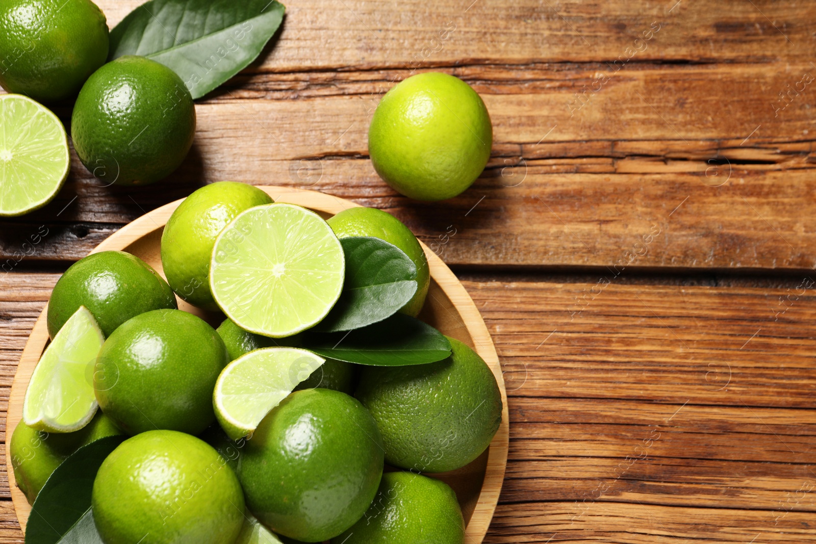 Photo of Fresh limes and green leaves on wooden table, top view. Space for text
