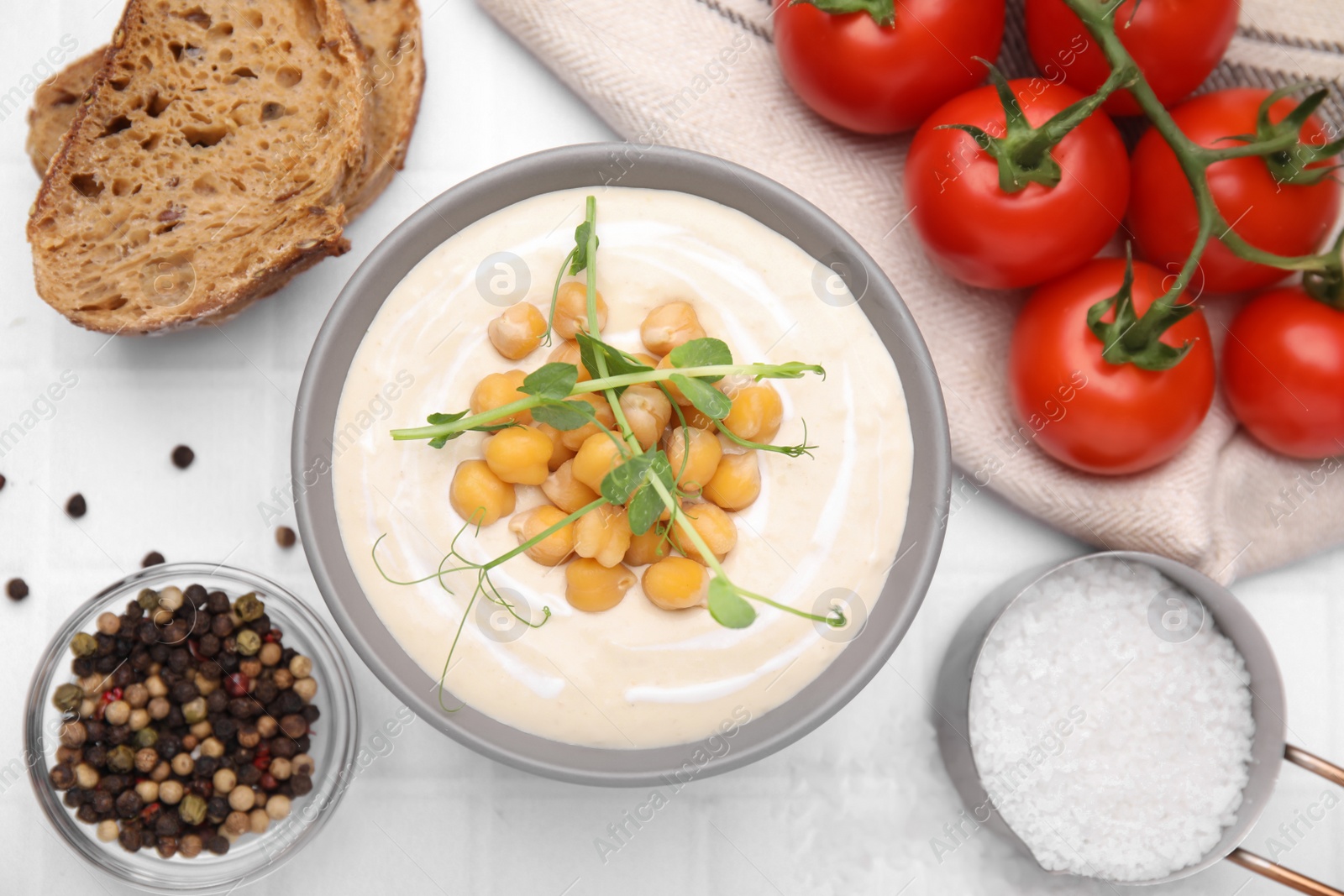 Photo of Flat lay composition of tasty chickpea soup in bowl on white tiled table