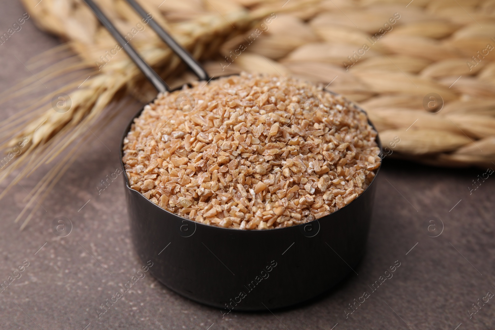 Photo of Dry wheat groats in scoop on brown table, closeup