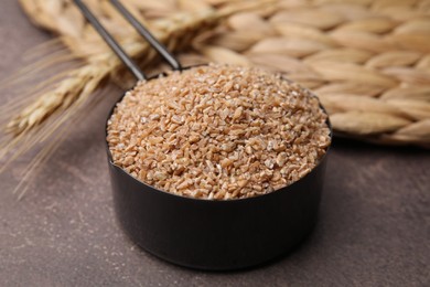 Dry wheat groats in scoop on brown table, closeup