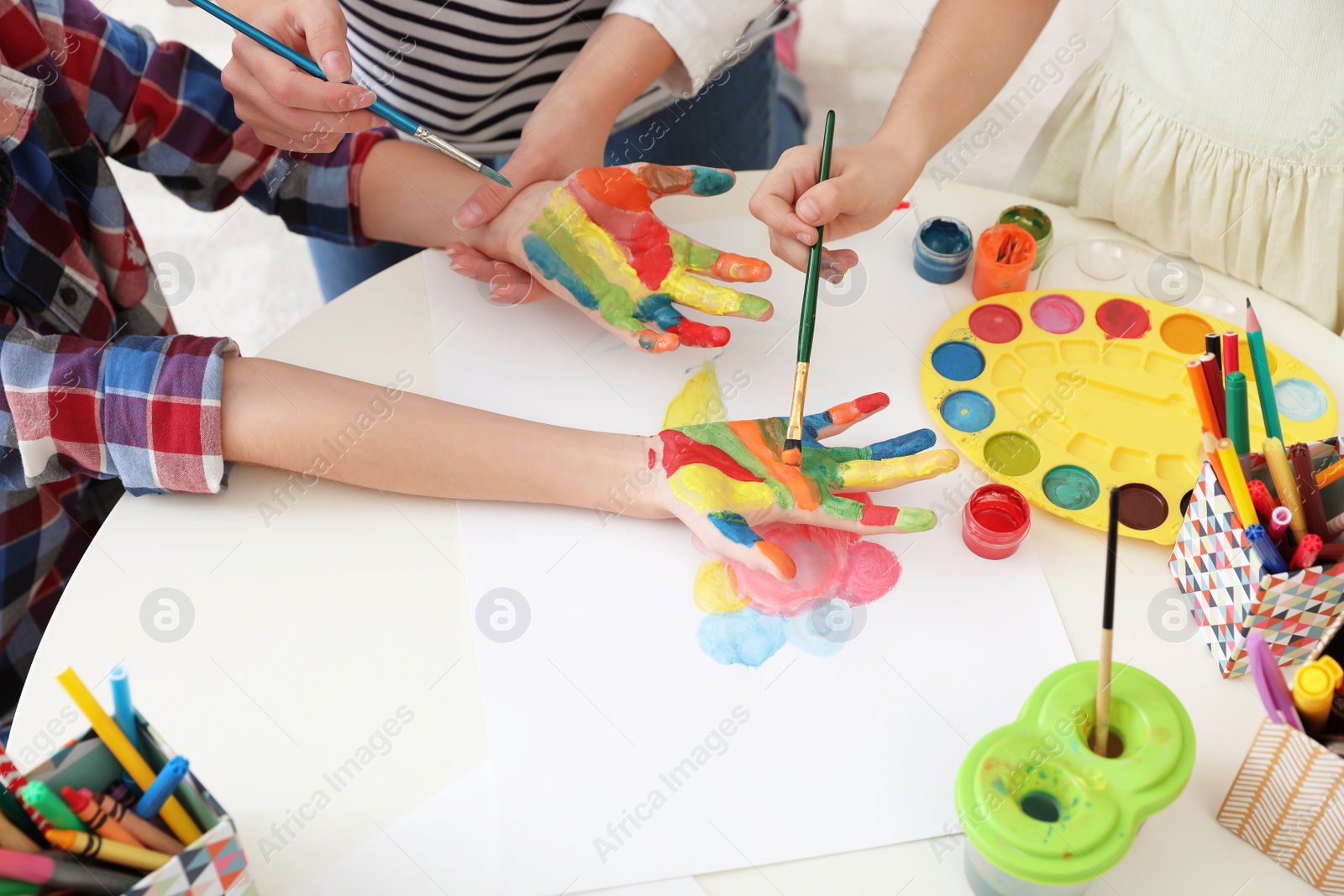 Photo of Young woman with children painting hands at table indoors, closeup view
