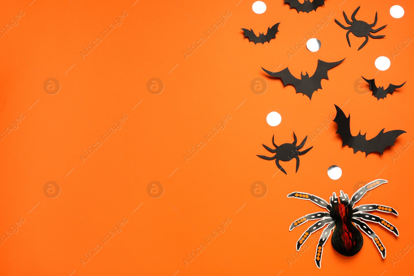 Photo of Flat lay composition with paper bats, spiders and golden confetti on orange background, space for text. Halloween celebration