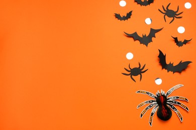 Flat lay composition with paper bats, spiders and golden confetti on orange background, space for text. Halloween celebration