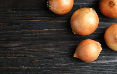 Photo of Ripe onions on black wooden table, flat lay with space for text