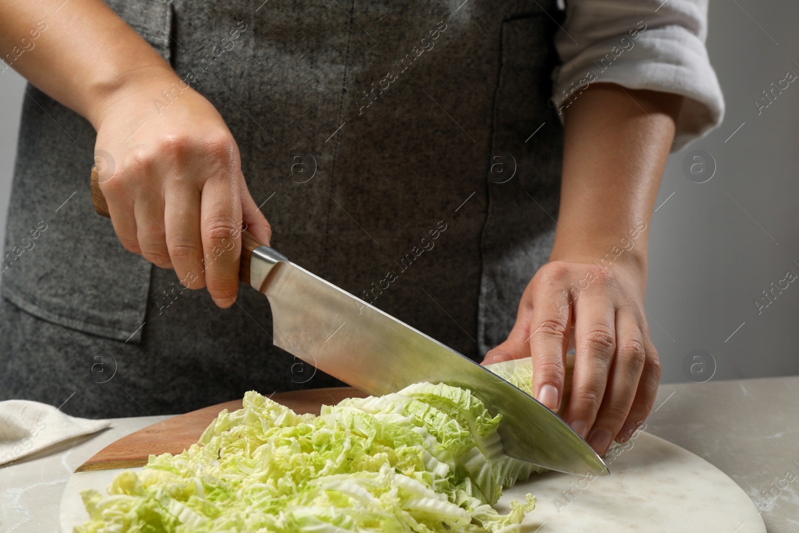 Photo of Woman cutting fresh Chinese cabbage at light grey table, closeup