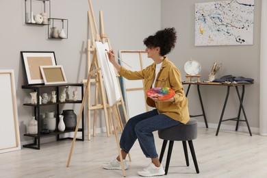 Photo of Young woman painting on easel with canvas in studio