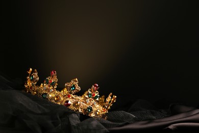 Photo of Beautiful golden crown with gems on dark cloth. Space for text
