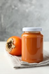 Photo of Delicious persimmon jam in glass jar and fresh fruit on white table