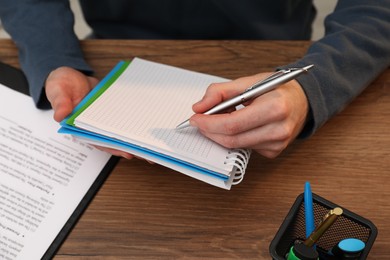 Photo of Man taking notes at wooden table, closeup