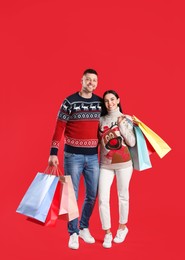 Photo of Happy couple with paper bags on red background. Christmas shopping