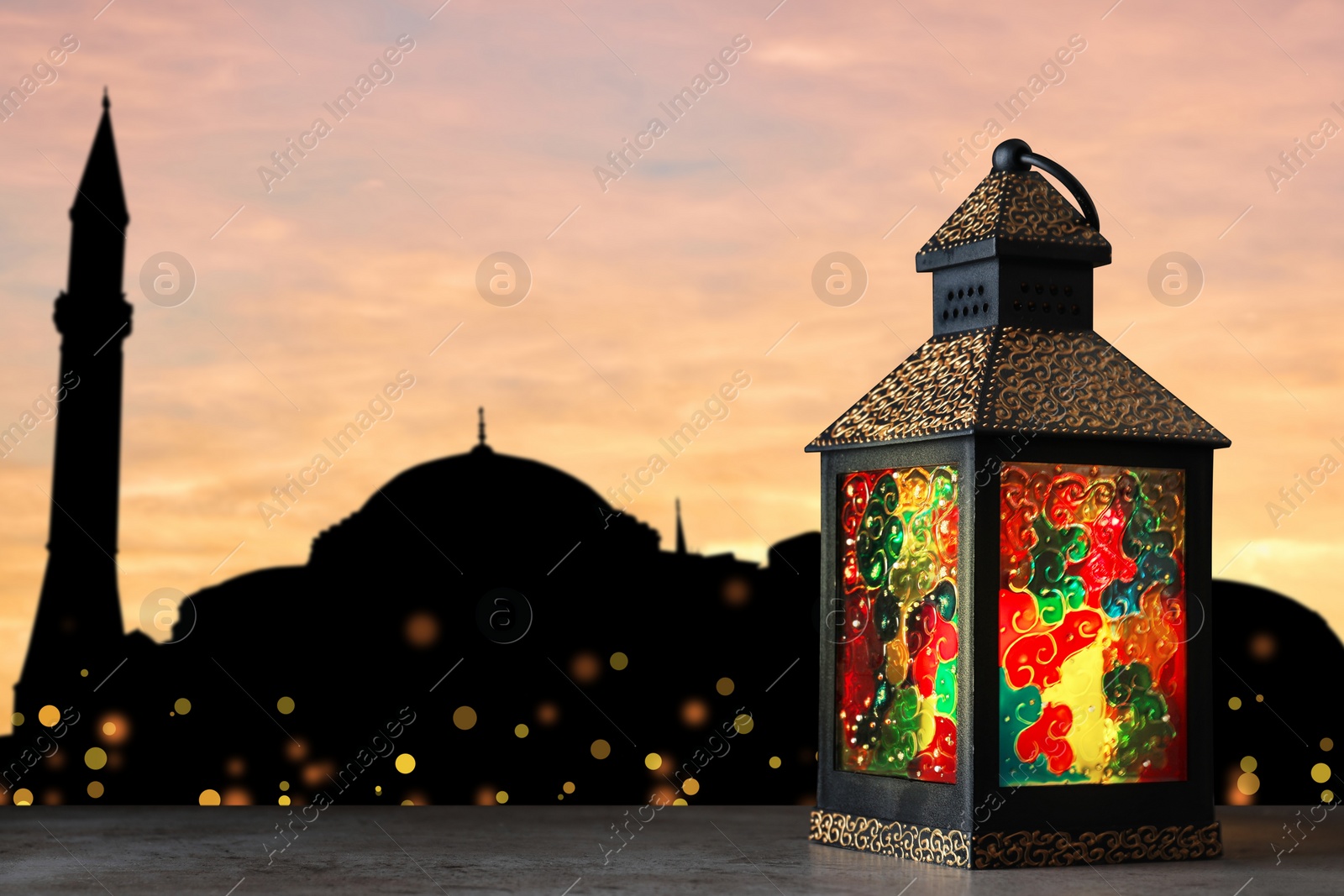 Image of Decorative Arabic lantern on stone surface and silhouette of mosque at sunset on background, space for text