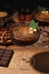 Dessert bowls of delicious hot chocolate and ingredients on wooden table, closeup