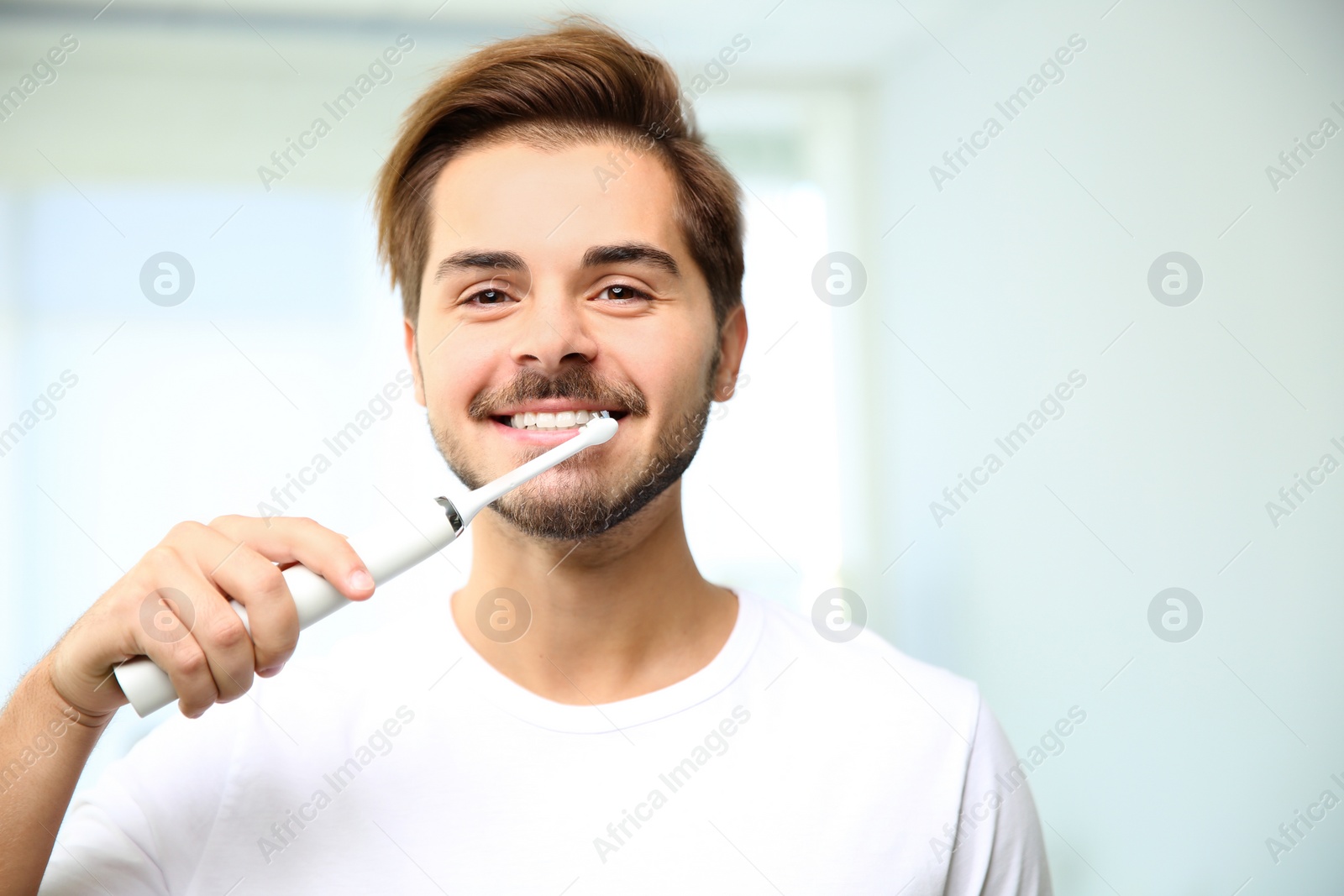 Photo of Portrait of young man with electric toothbrush on blurred background. Space for text