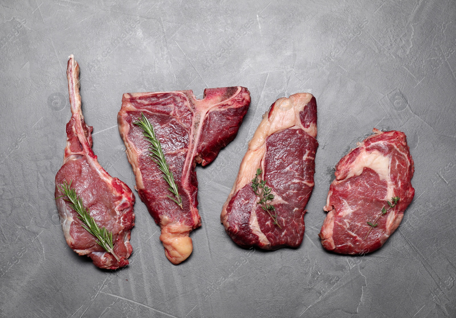 Photo of Fresh raw beef cuts with herbs on light grey textured table, flat lay