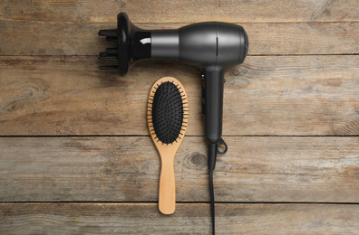 Photo of Hair dryer and brush on wooden table, flat lay. Professional hairdresser tool