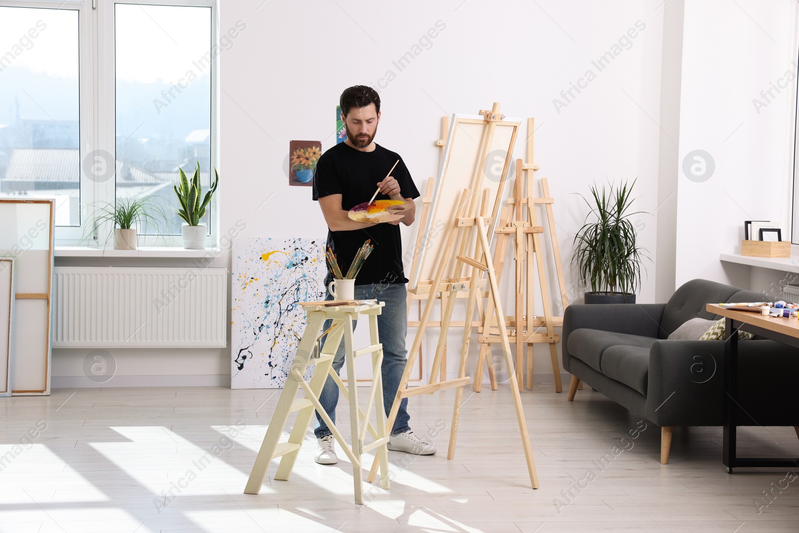 Photo of Man painting in studio. Using easel to hold canvas