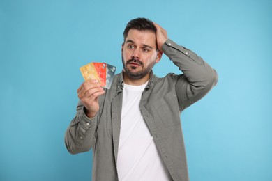 Confused man with credit cards on light blue background. Debt problem