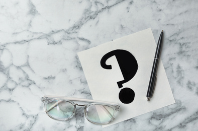 Photo of Note with question mark, eyeglasses and pen on white marble table, flat lay. Space for text